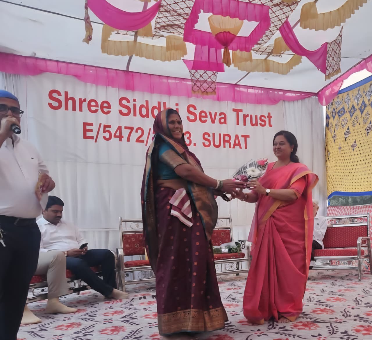 A woman being honoured with flowers at a Shree Siddhi Seva Trust community programme
