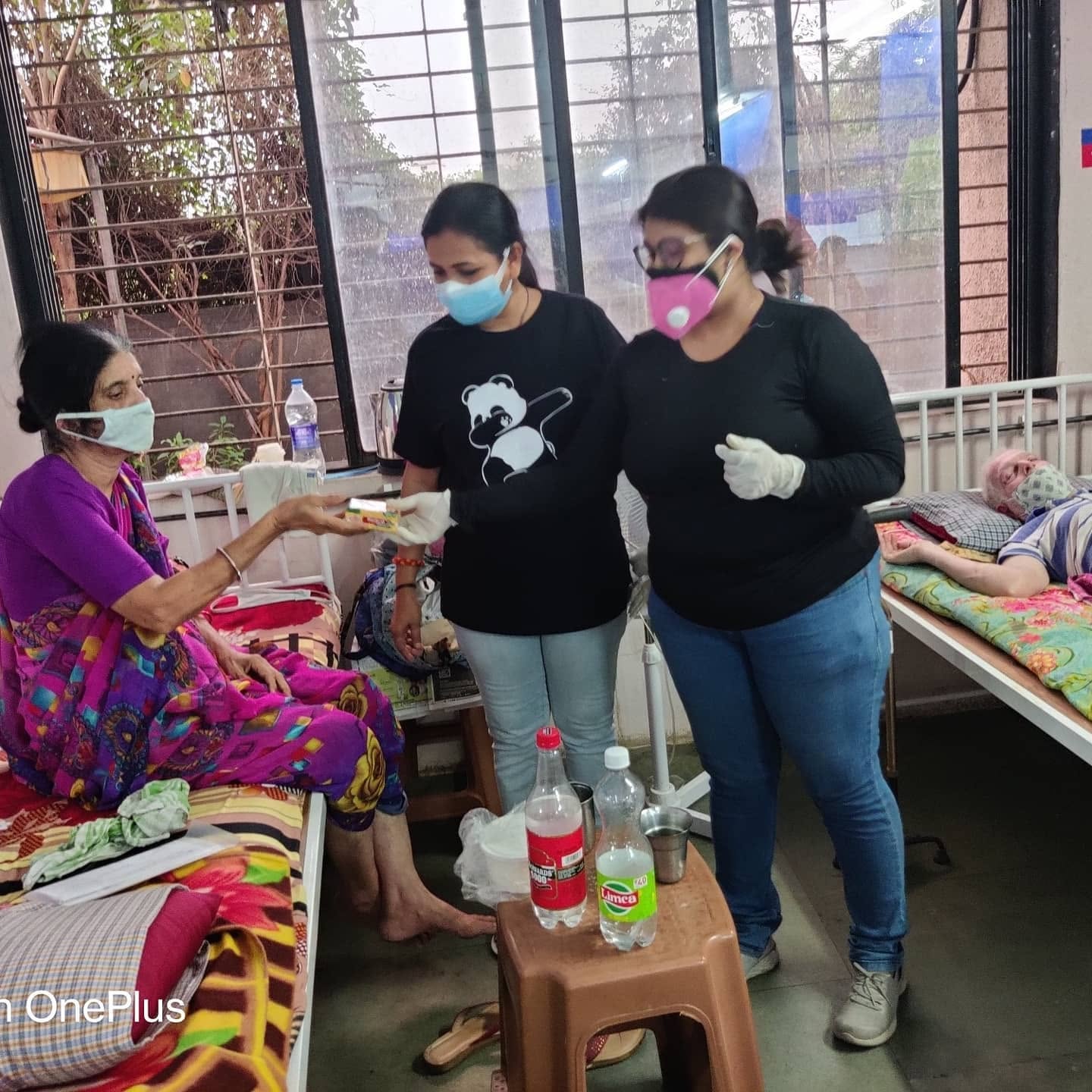 A masked volunteer handing medicine to a patient at a COVID care centre