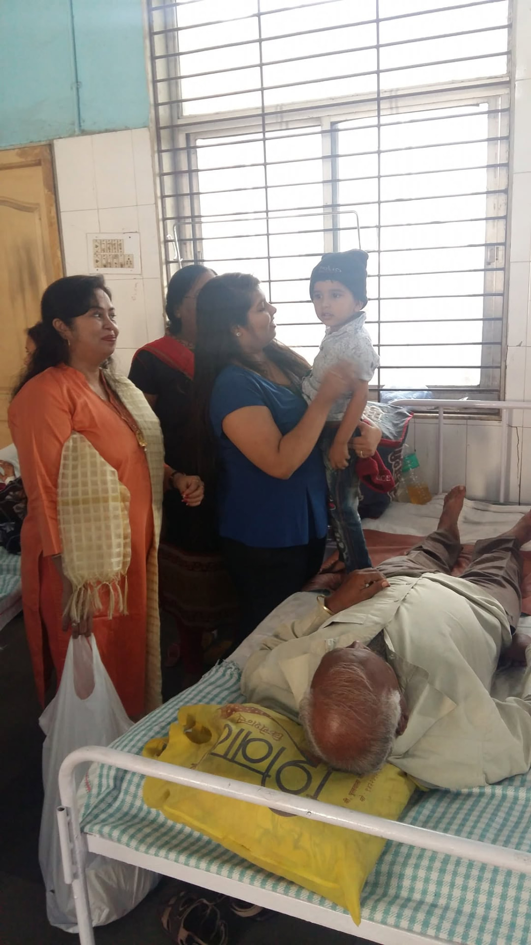 A volunteer holding a toddler wearing a new winter cap in a hospital ward